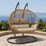 Balançoire Orvella design 2 places avec coussin beige sur terrasse moderne, cadre métal noir et panier en rotin synthétique