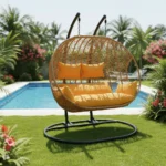 Balançoire Orvella 2 places avec coussin jaune dans un jardin, cadre métal noir et panier en rotin synthétique