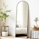 miroir Arco rectangulaire avec cadre métallique antirouille et sommet cintré, vue légèrement de côté dans une chambre à coucher moderne et élégante