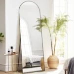 miroir rectangulaire sur pied avec cadre métallique antirouille et sommet cintré, vue légèrement de côté, design moderne pour chambre ou salon